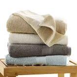 A stack of four folded towels in neutral and pastel colors sits on a wooden surface.