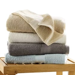 A stack of four folded towels in neutral and pastel colors sits on a wooden surface.