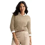 A woman is wearing a beige cable-knit sweater over a white collared shirt, paired with beige high-waisted pants and a brown belt.