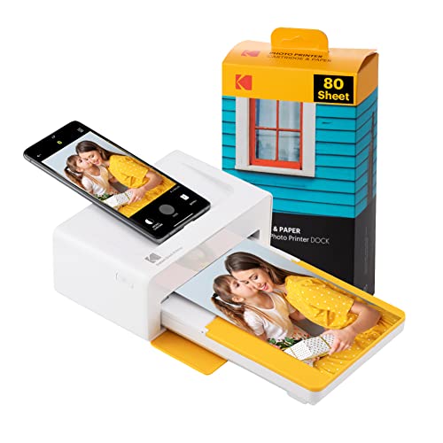 A white and yellow Kodak photo printer dock with a smartphone on top displaying a photo, accompanied by an 80-sheet pack of 4x6 photo paper.
