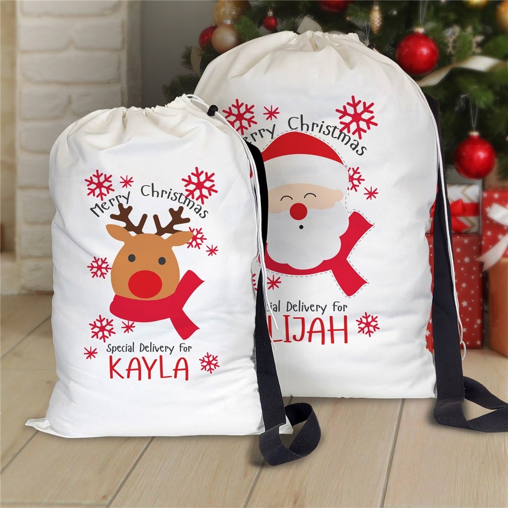 Two Christmas-themed drawstring gift bags, one featuring a reindeer design labeled \“Special Delivery for KAYLA\“ and the other with a Santa design labeled \“Special Delivery for ELIJAH,\“ are placed in front of a Christmas tree.