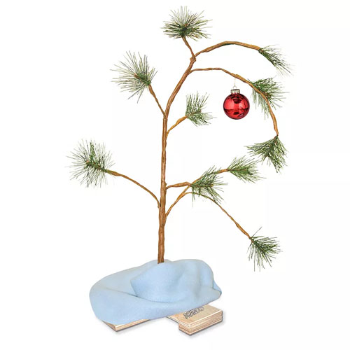 A small, sparse Christmas tree with a single red ornament, resembling the iconic tree from \“A Charlie Brown Christmas,\“ mounted on a wooden stand with a blue blanket at the base.