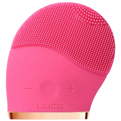 A pink silicone facial cleansing brush with two buttons marked \“-\“ and \“+\“, featuring soft bristles for exfoliating and cleaning the skin. The word \“LUCE\“ is embossed on its front.