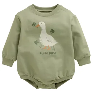 A green baby bodysuit features a duck and clovers illustration with the text \“Lucky Duck.\“ It has long sleeves and snap buttons at the bottom.