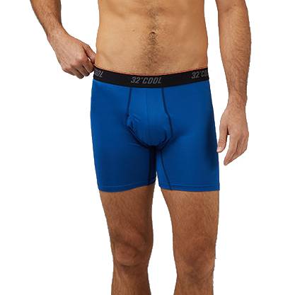 A man models orange boxer briefs with a black waistband featuring the \“32° COOL\“ brand, standing barefoot against a gray background.