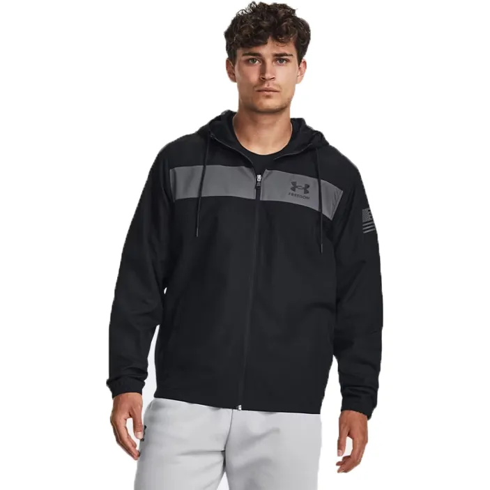The UA Freedom Hooded Windbreaker is a lightweight, black jacket with a gray chest stripe and a zip front, featuring the Under Armour logo and \“Freedom\“ text. It has adjustable drawstrings on the hood and an American flag patch on the sleeve.