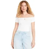 A woman is wearing a white off-the-shoulder top with a scalloped neckline and light blue high-waisted jeans.