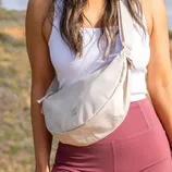 A woman wearing a white tank top and maroon leggings carries a beige crossbody bag with the \“Got Bag\“ logo.