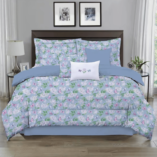 A floral-patterned bedding set with a light blue base includes a comforter, pillow shams, and decorative pillows, arranged on a bed in a modern bedroom setting.