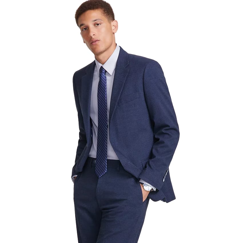 Nautica Men's Suit features a navy blue color with a slim, modern fit. It includes a two-button jacket and matching pants, paired with a light blue dress shirt and a patterned blue tie for a classic, professional look.