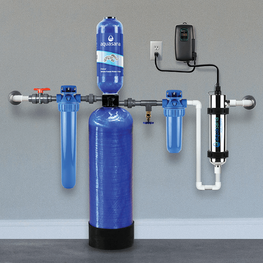 A whole house water filtration and UV purification system by Aquasana, featuring multiple blue filtration components and a connected electronic control device, mounted on a wall.