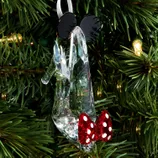 A clear high-heeled shoe ornament with black mouse ears and a red polka-dot bow hangs on a Christmas tree branch.