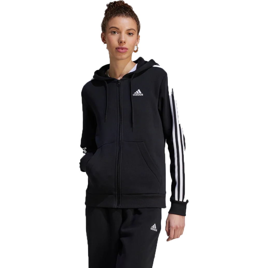 A woman wearing a black Adidas zip-up hoodie with white stripes on the sleeve and matching track pants.