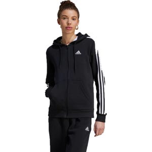 A woman wearing a black Adidas zip-up hoodie with white stripes on the sleeve and matching track pants.