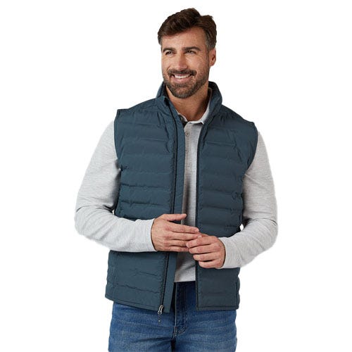 A man is wearing a padded, teal-colored vest over a light gray long-sleeve shirt, paired with blue jeans.