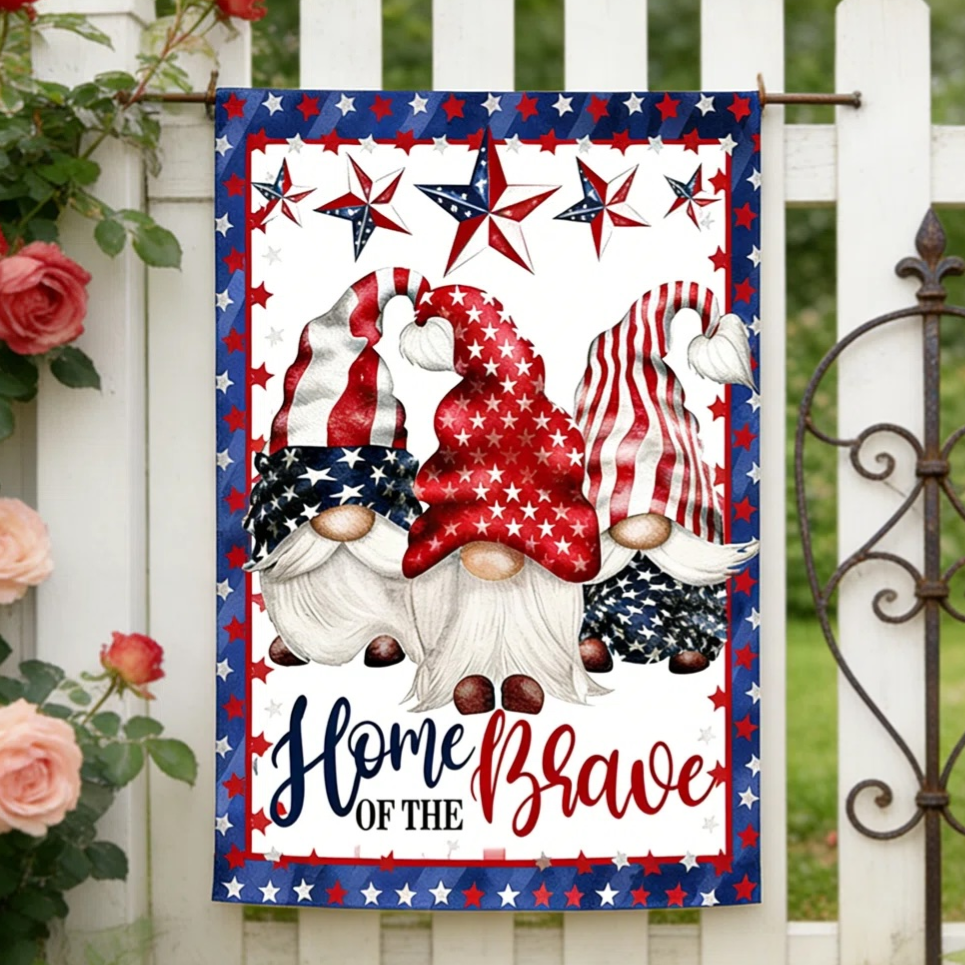A garden flag featuring patriotic gnomes in red, white, and blue star-themed hats with the text \“Home of the Brave,\“ displayed on a white picket fence surrounded by roses.