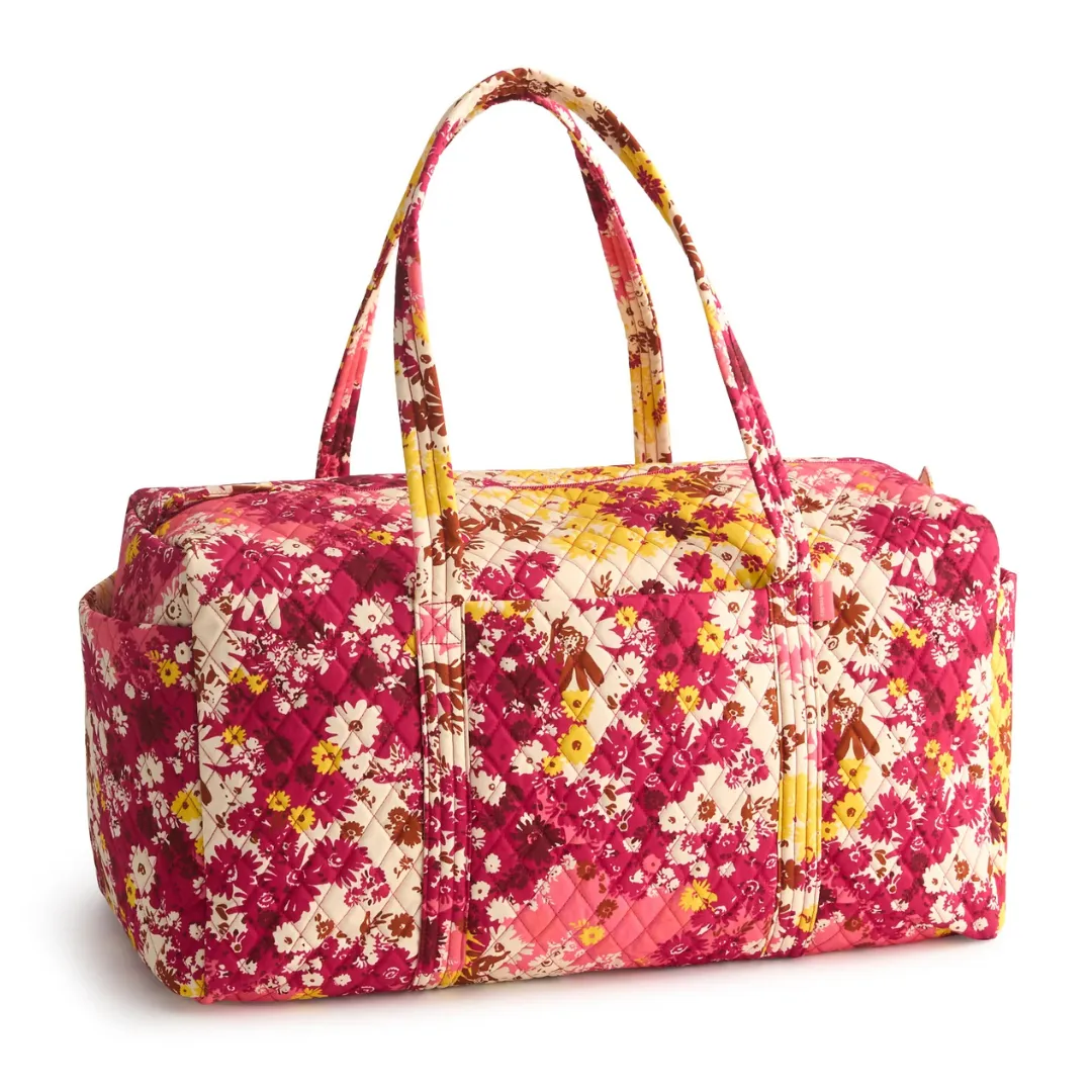 A quilted floral-patterned duffle bag featuring vibrant pink, yellow, and brown tones with two sturdy handles, suitable for travel or leisure.