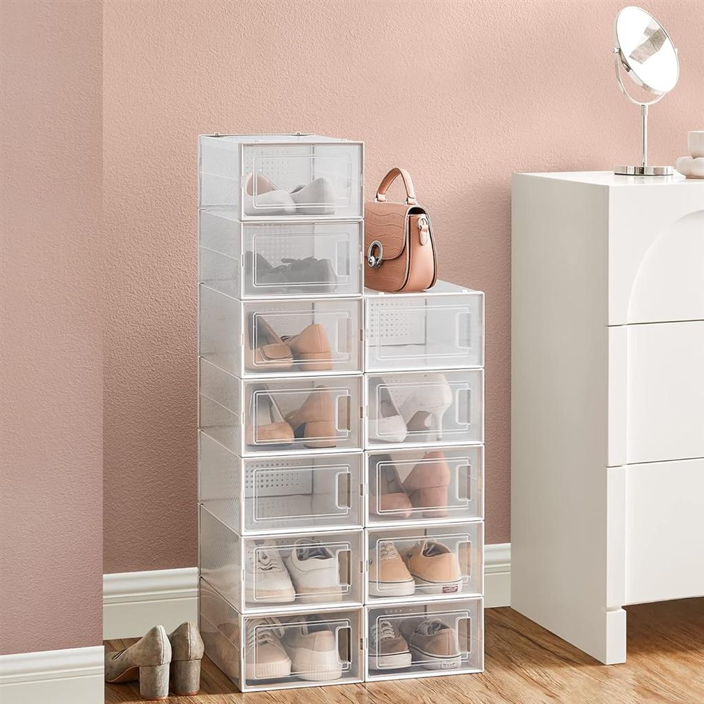 A tower of clear, stackable shoe storage boxes with a small pink handbag on top, placed next to a white cabinet with a mirror.