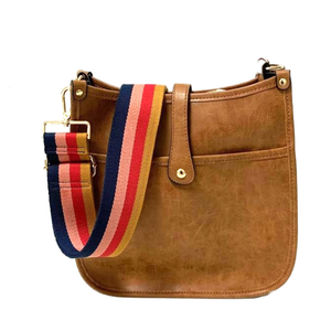 A brown faux-leather courier bag with a front pocket and a flap closure secured by a gold button. It features a colorful, detachable shoulder strap with stripes in navy, red, pink, and mustard.