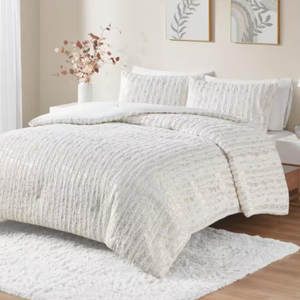 A bedroom with a textured white bedding set on a bed, a matching rug, and decorative wall art.