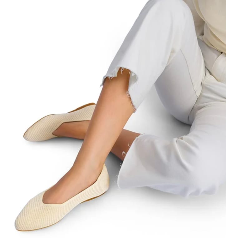 A person wearing beige flat shoes and white ripped-hem jeans.