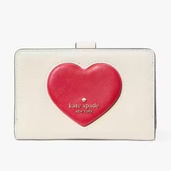 A compact cream-colored wallet featuring a prominent red puffy heart design, emblazoned with the \“kate spade new york\“ logo on the front.