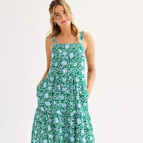 A woman wearing a green floral dress with wide straps and tiered skirt.
