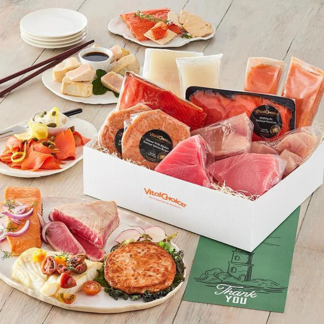 An assortment of seafood including packaged salmon, tuna, fish fillets, and fish burgers from \“Vital Choice,\“ accompanied by plates featuring smoked salmon, sashimi, and garnishes.
