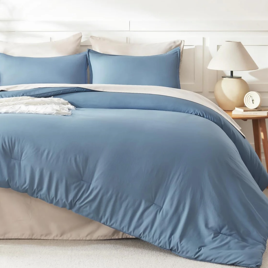 A bed features a blue and beige bedding set with matching pillows, a bedside table, and a lamp.