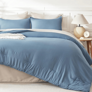 A bed features a blue and beige bedding set with matching pillows, a bedside table, and a lamp.