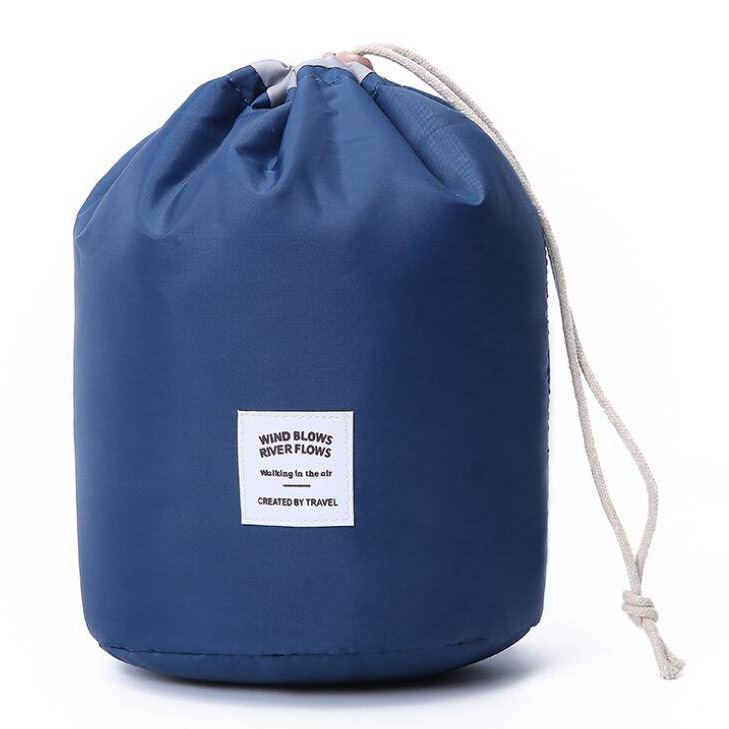A blue cylindrical drawstring bag with a simple design, featuring a white square patch that reads \“WIND BLOWS RIVER FLOWS Walking in the air CREATED BY TRAVEL.\“