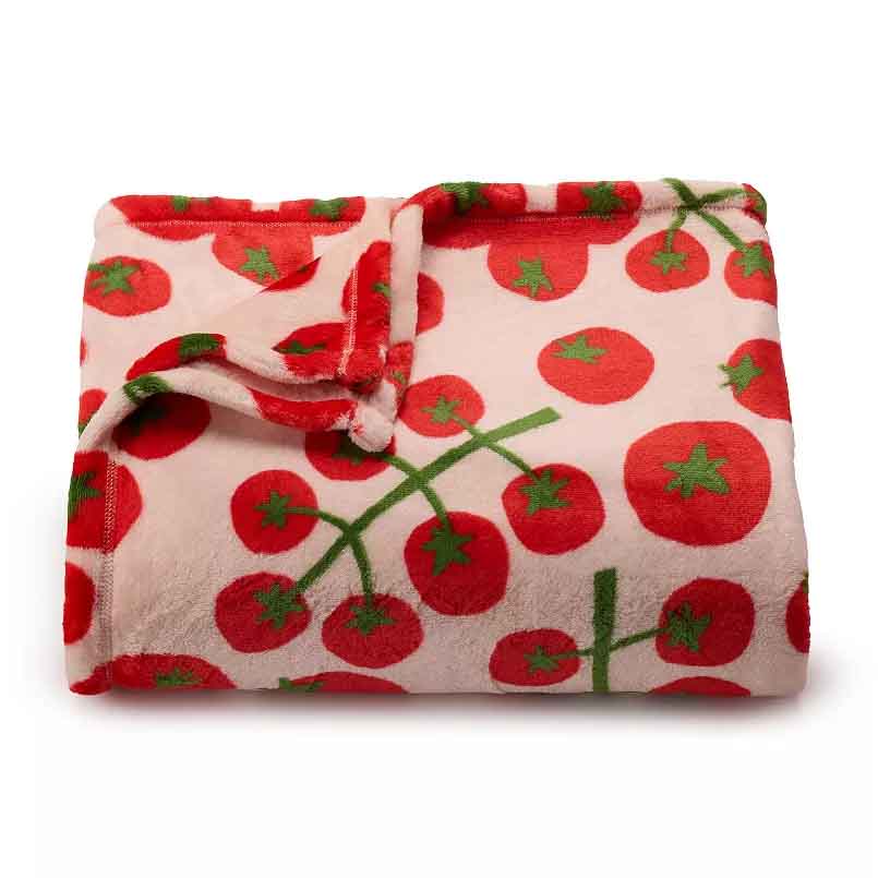 Fleece blanket with a pattern of red tomatoes on green vines against a light background.