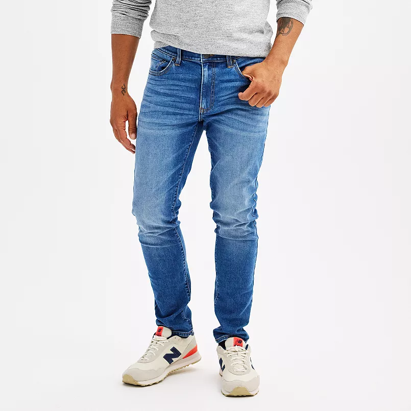 A man wearing light blue jeans and white sneakers with blue and red accents.