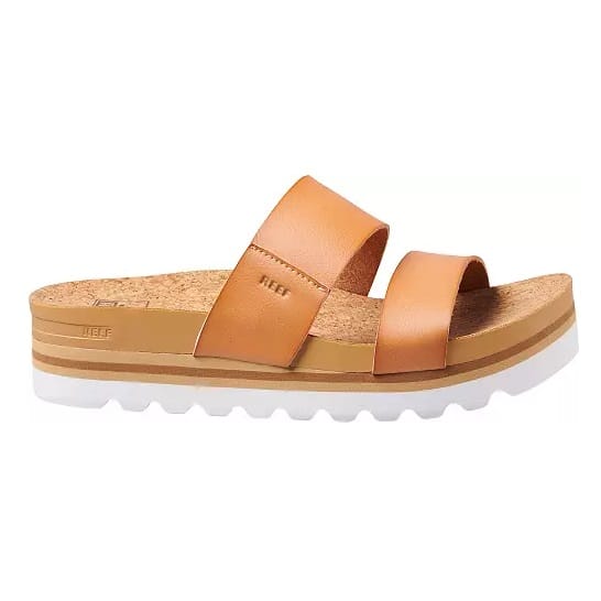 Tan slide sandals with two straps and a cork sole, accented by a white jagged outsole.