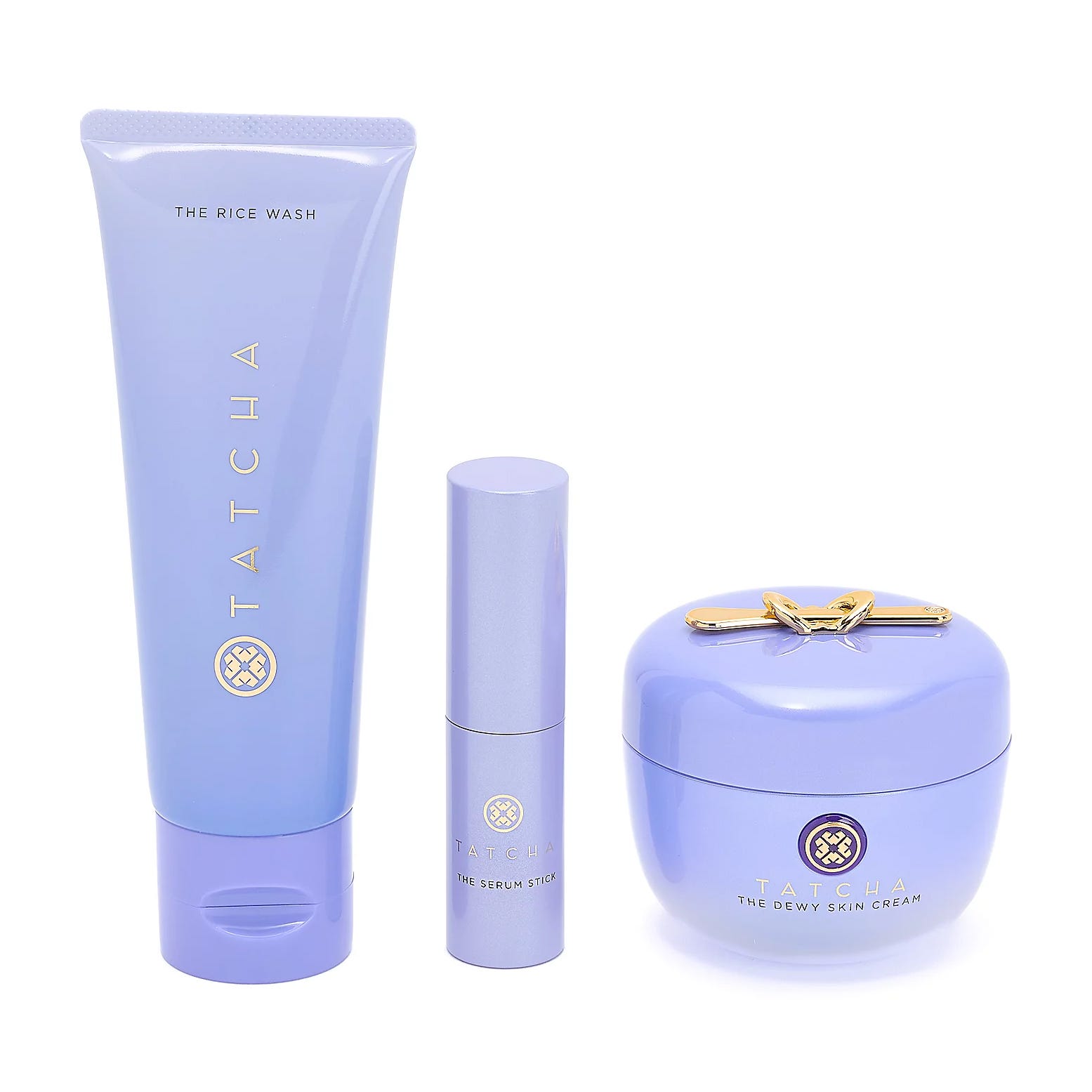 Tatcha skincare set with three items: The Rice Wash (cleanser), The Serum Stick (hydrating treatment), and The Dewy Skin Cream (moisturizer), all in lavender packaging with gold accents.