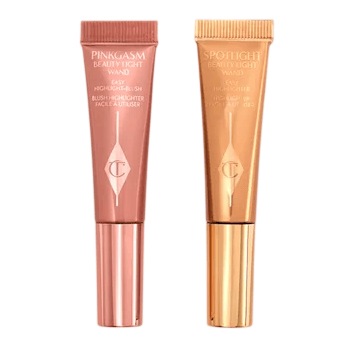 Two tubes of Charlotte Tilbury Beauty Light Wand are shown: Pinkgasm, a pink blush highlighter, and Spotlight, a gold highlighter.