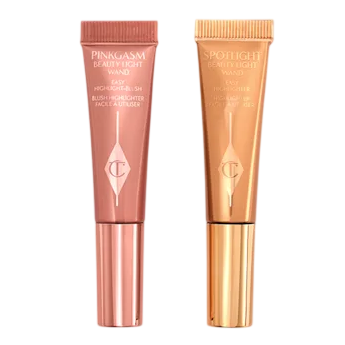 Two tubes of Charlotte Tilbury Beauty Light Wand are shown: Pinkgasm, a pink blush highlighter, and Spotlight, a gold highlighter.