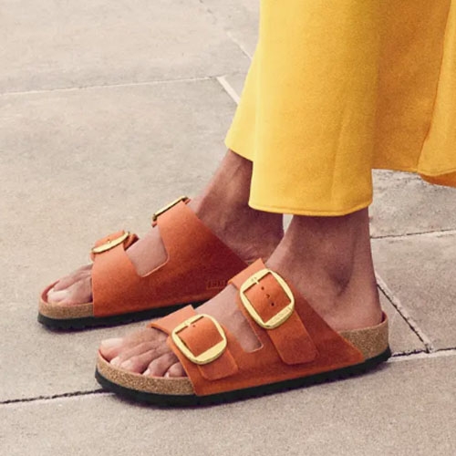 Person wearing tan sandals with two buckles and a yellow garment.