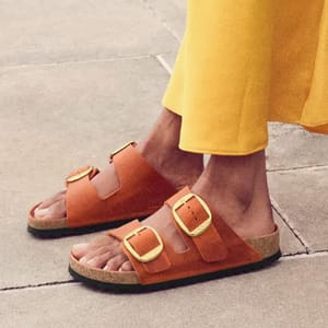 Person wearing tan sandals with two buckles and a yellow garment.