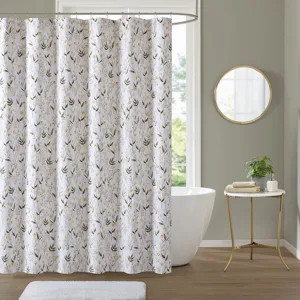 Floral shower curtain with a subtle pattern, alongside a white bathtub, round mirror, small table with plant, and towels, on a light wooden floor.