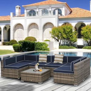 Outdoor wicker sofa set with navy cushions, including an L-shaped sectional and a matching coffee table, placed beside a modern villa with a pool.