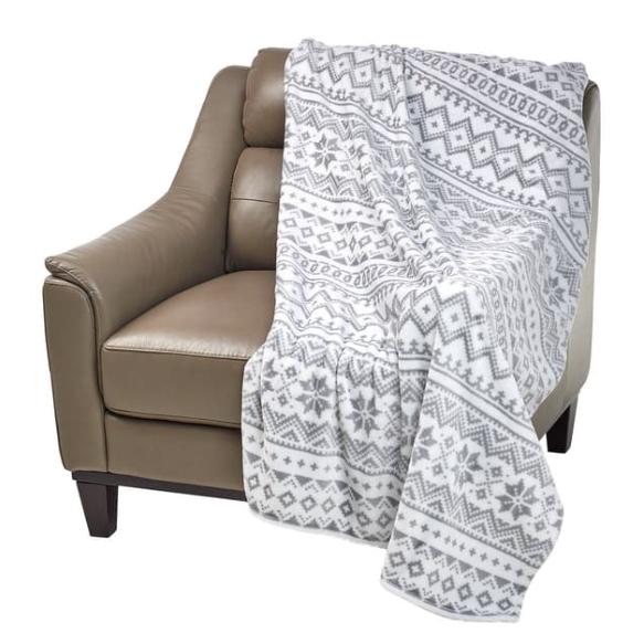 A plush throw featuring a Nordic winter design with snowflakes and geometric patterns in grey and white, draped over a brown leather armchair.