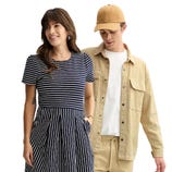 A woman wearing a navy and white striped dress stands beside a man in a beige shirt jacket, white T-shirt, jogger pants, and a beige cap.