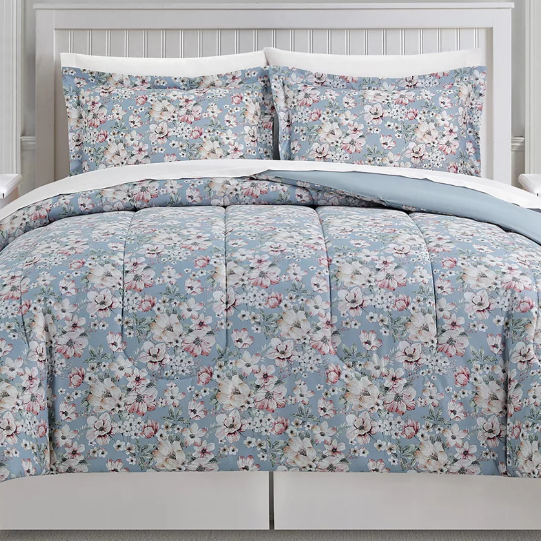 A floral-patterned bedding set with a comforter and two pillow shams on a bed with a white headboard. The design features pastel blue, pink, and white flowers.