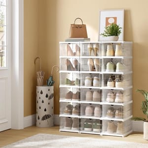 Transparent shoe storage boxes are stacked in a room, with umbrellas in a decorative holder and a potted plant on top.