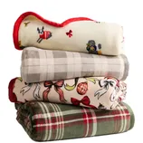 A stack of four folded blankets featuring different patterns: white with dogs and red trim, beige plaid, cream with bows and holiday motifs, and green plaid with red accents.