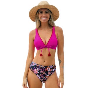 Woman wearing a pink bikini top with tassels, floral high-waisted bottoms, and a straw hat.