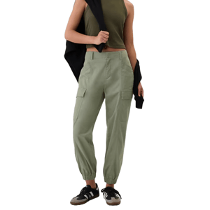Olive green cargo joggers with elasticized cuffs, side pockets, and a relaxed fit. Paired with a cropped olive tank top, a black jacket draped over one shoulder, and black sneakers.