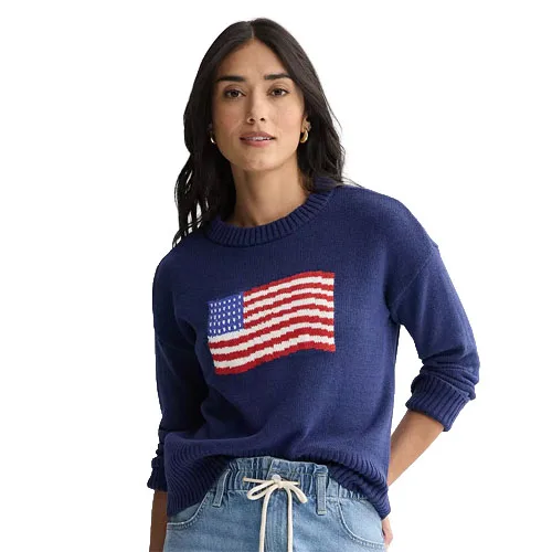A woman is wearing a blue sweater featuring an American flag design, paired with light blue jeans.