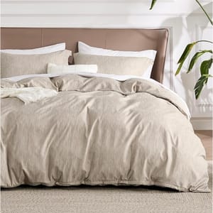 A beige 3-piece Queen Duvet Cover Set includes a duvet cover and two pillow shams, featuring a subtle textured pattern. The set is displayed on a neatly made bed with a beige and white color scheme, accented by a plant in the background.